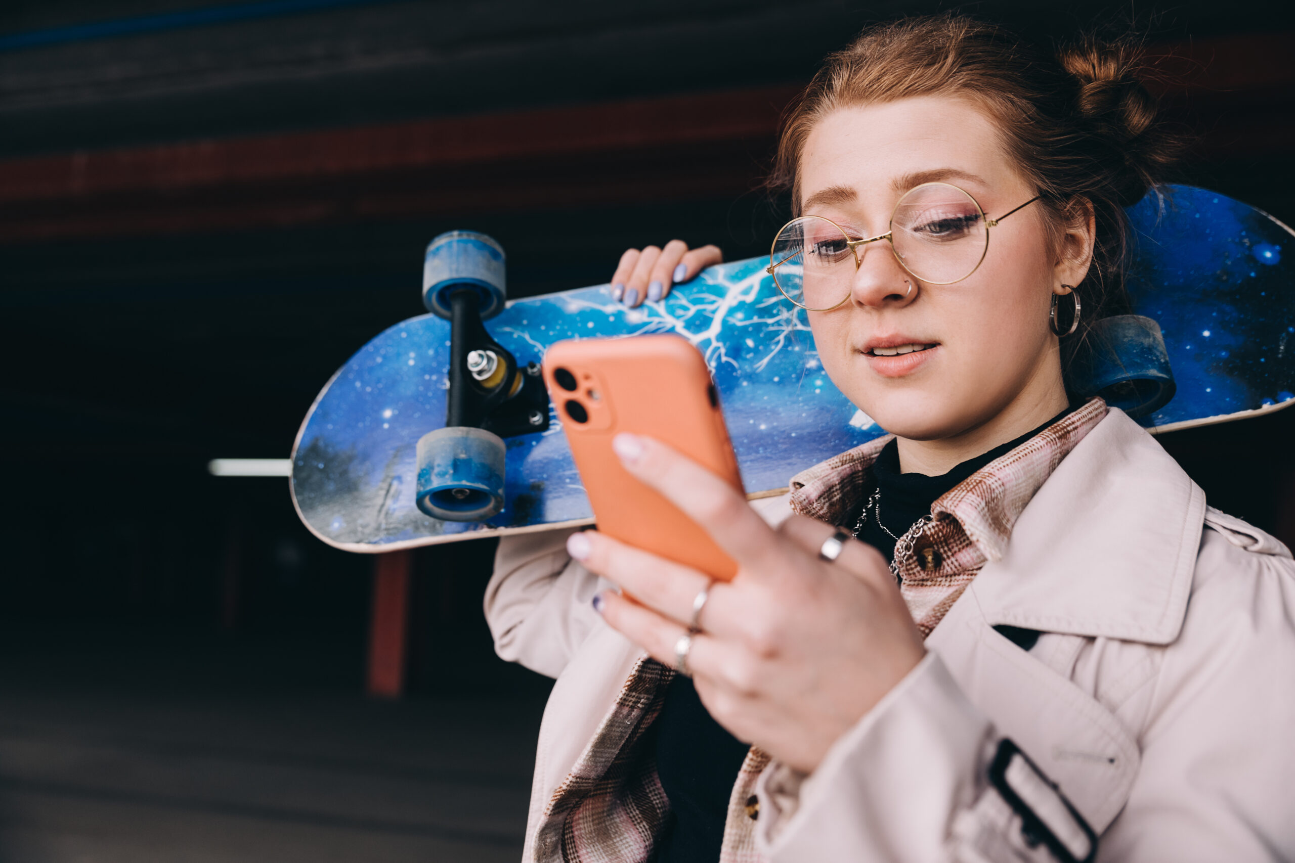 young caucasian woman with a skateboard, in the parking lot uses a smartphone checks messages and texting with friends